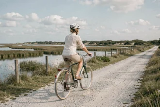 Cycliste femme pédalant sur une piste côtière près de La Cotinière sur l'île d'Oléron, avec marais salants et ciel atlantique